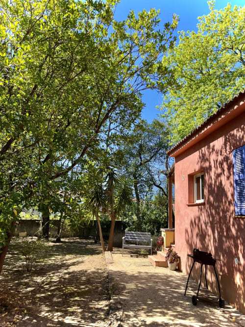 Villa en terre cuite au Maquis Plage avec arbres verdoyants, cour sablonneuse et volets bleus à Poggio-Mezzana