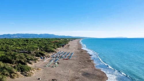 Spiaggia sabbiosa con ombrelloni blu lungo la costa toscana vicino a Pomarance, montagne sullo sfondo
