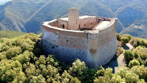 Fortezza medievale circondata da colline verdi presso Pomarance, Italia, vista aerea con paesaggio boscoso