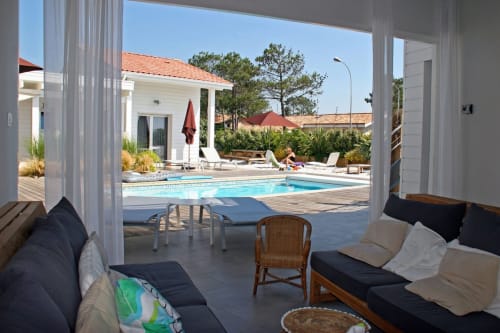 Hôtel Côte et Dune à Biscarrosse Plage : élégant espace détente bord piscine avec vue océan, piscine bleue, colonnes blanches et mobilier