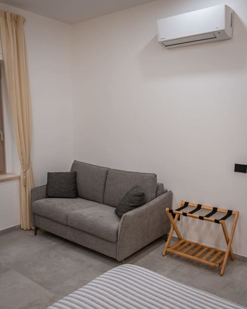 Modern apartment at Museo19 Naples with gray sofa, wooden luggage rack, and wall-mounted AC unit