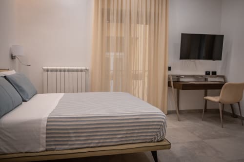 Modern bedroom at Museo19 apartment in Naples with striped bedding, desk, TV, and natural light from sheer curtains
