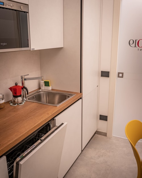 Modern apartment kitchen at Museo19 in Naples with wooden countertop, stainless sink, dishwasher, and white cabinetry