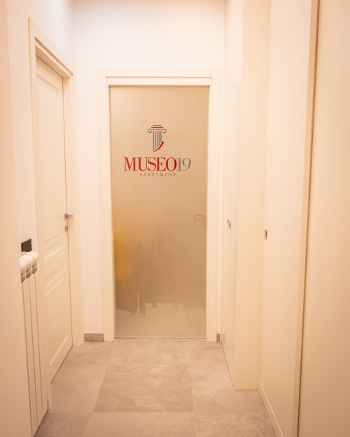 Museo19 apartment hallway in Naples with cream walls and glass door entrance