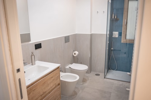 Modern bathroom at Museo19 apartment in Naples with white sink, toilet, bidet, and blue tile shower enclosure