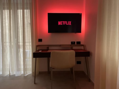 Modern Home apartment at Museo19 Naples with desk, chair, and wall-mounted TV displaying Netflix logo with red ambient