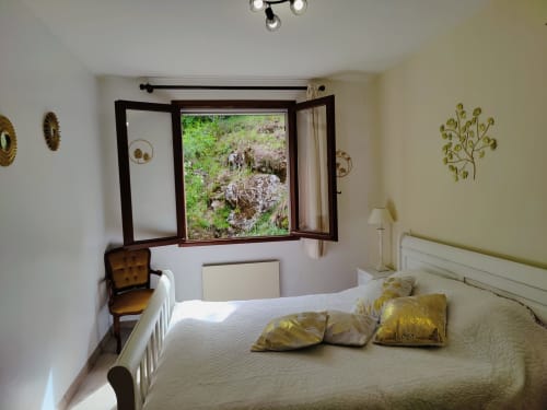 Chambre à Location MarjoRI avec vue sur les montagnes par la fenêtre ouverte, literie crème et touches dorées