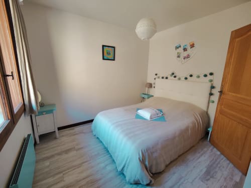 Chambre lumineuse à Location MarjoRI avec accents turquoise, lit en bois, suspension blanche et vue montagne