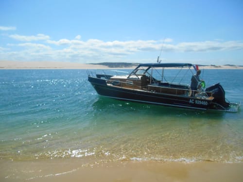 Bateau de pêche noir et vert mouillé dans les eaux turquoise peu profondes de la plage de Biscarrosse