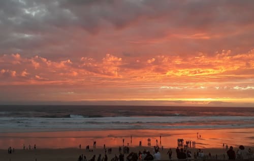 Coucher de soleil spectaculaire sur la plage de Biscarrosse avec foules profitant de l'heure dorée et des vagues océaniques