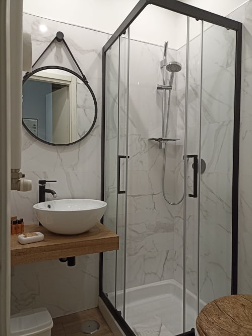 Bagno moderno presso AD Trastevere Guest House Roma con doccia in marmo, specchio rotondo e mobile lavabo in legno