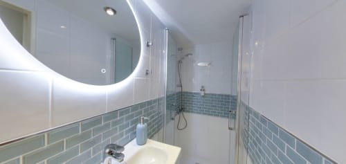 Modern bathroom in Exotic Berry room at Aux Prés Du Berry with LED mirror, blue subway tile, glass shower, and white fixtures