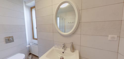 Modern bathroom in Berry Nature room at Aux Prés Du Berry with oval mirror, white sink, and beige tile walls