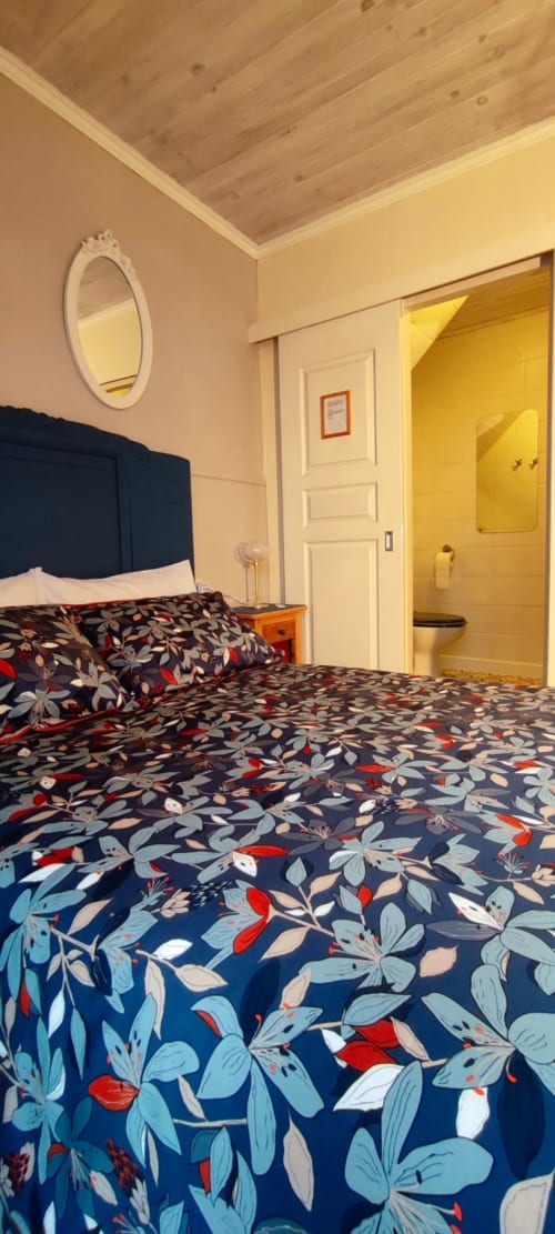 Bedroom at Aux Prés Du Berry with dark floral bedding, navy headboard, wooden ceiling, and ensuite bathroom with yellow walls