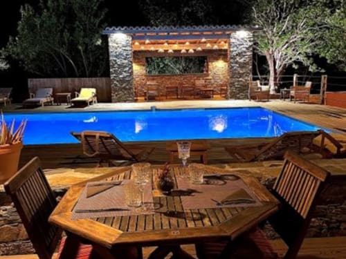 Piscine illuminée du Le Maquis Plage avec table de restaurant, transats et établissement en pierre à Poggio-Mezzana