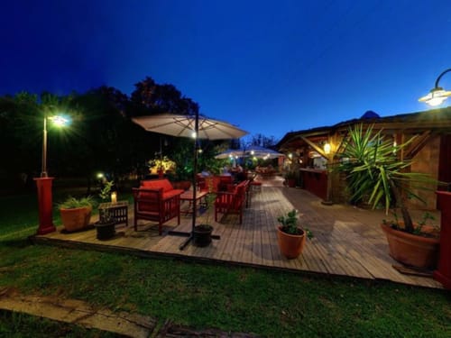 Terrasse de l'hôtel Le Maquis Plage au crépuscule avec sièges rouges, parasols et plantes tropicales à Poggio-Mezzana