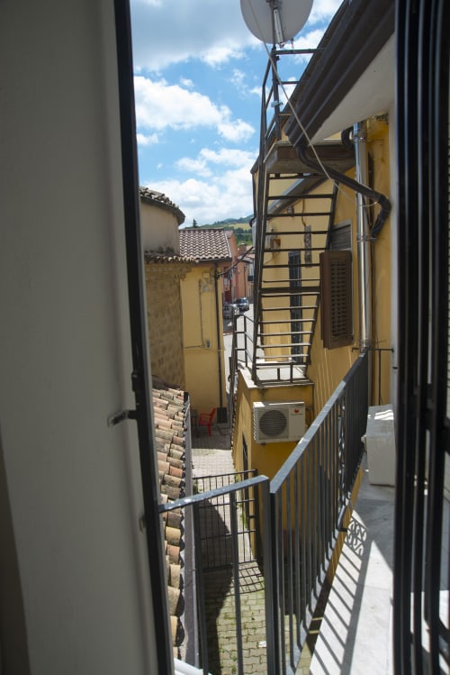 Vicolo stretto presso il B&B La Pigna a Filiano con edificio giallo, ringhiera metallica e vista sulla campagna toscana