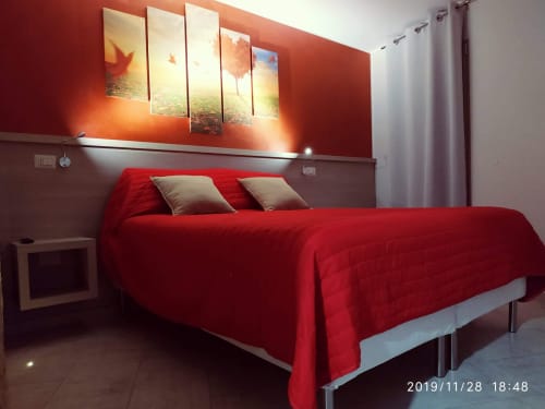 Camera da letto rossa brillante a La Pigna in Filiano con letto moderno, cuscini beige e arte murale al tramonto
