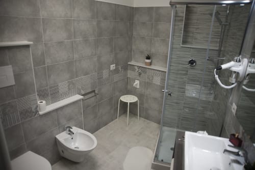 Moderno bagno del B&B La Pigna a Filiano con pareti rivestite in piastrelle grigie, bidet bianco, lavandino, doccia e WC
