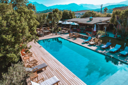 La piscine de l'hôtel Le Maquis Plage à Poggio-Mezzana avec eau turquoise, transats et montagnes