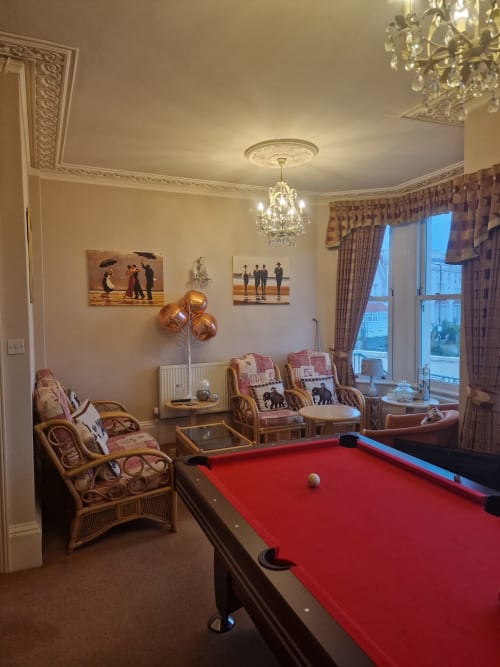 Elegant games room at The Sands Hotel Paignton featuring red pool table, rattan chairs, crystal chandelier, and seaside views