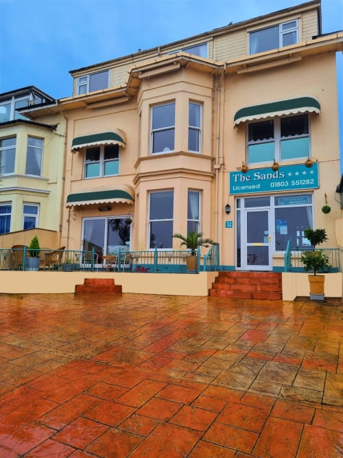 The Sands Hotel in Paignton, a beige seafront building with bay windows, green awnings, and terracotta patio