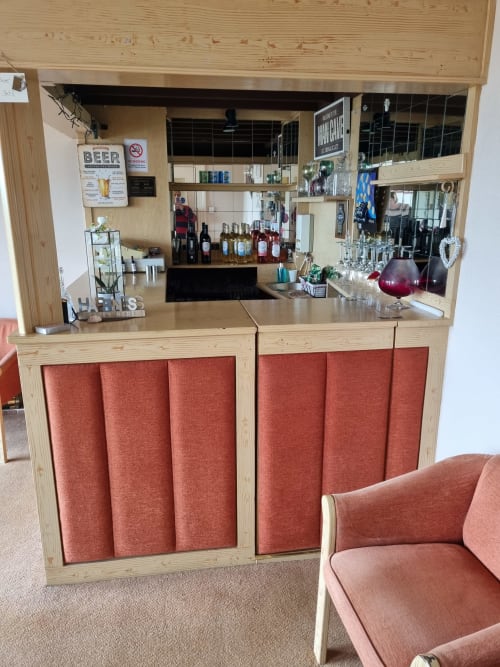 The Sands Hotel bar with light wood counter, red fabric panels, bottles, glassware, and decor in Paignton