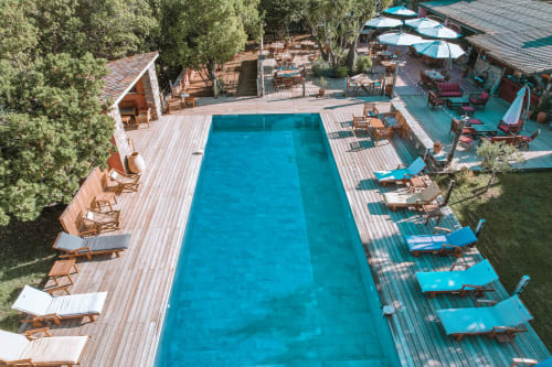 Vue aérienne de la piscine du Maquis Plage avec terrasse en bois, transats et parasols à Poggio-Mezzana