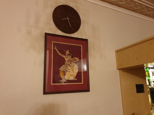 Dark round clock above framed Thai artwork in The Sands Hotel Paignton hallway