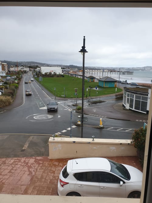 The Sands Hotel, Paignton. Elevated view of beach seafront with parked car, street lamp, green lawn and seaside buildings