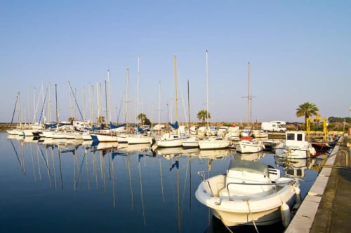 Barche a vela ormeggiate nelle acque tranquille della marina Torre Grande, Oristano, Italia con palme