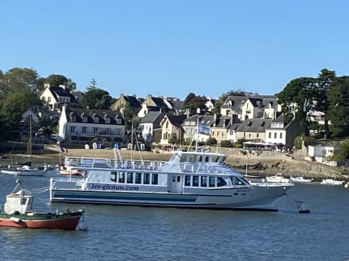 Traversier bleu et blanc amarré à Clohars-Fouesnant avec maisons en pierre traditionnelles le long du front de mer en Bretagne