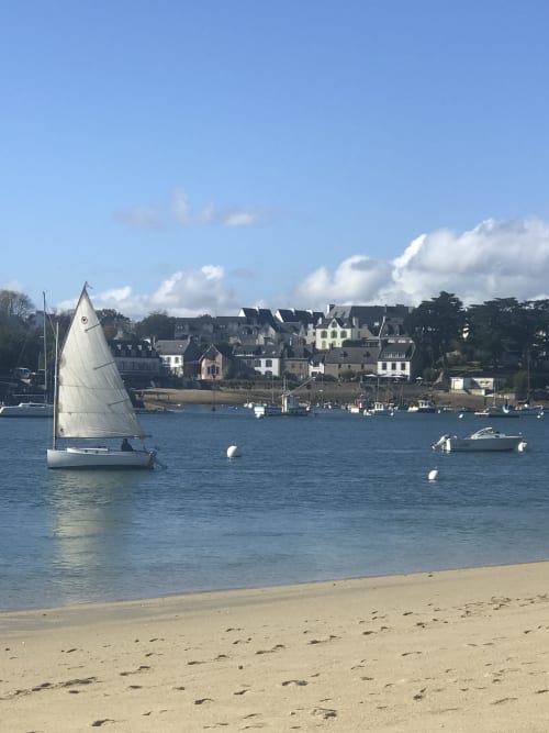 Voilier sur l'eau bleue près de la plage de sable fin et des maisons côtières de Clohars-Fouesnant, Bretagne