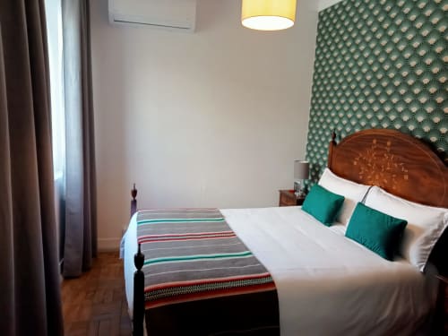 Bedroom at Patio Da Villa guest house in Coruche with wooden bed, teal headboard wallpaper, green pillows, and striped throw