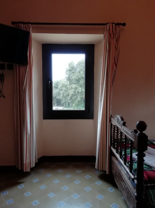 Habitación Rabassola|Sant Martí de Centelles-Alcoba particularmente diáfana y espaciosa, situada en la planta noble de la masía, con celosas vistas a la entrada principal de la masía y al distintivo reloj de estilo noucentista. Preparado para acoger cómodamente a familias, dispone de dos camas de madera maciza; uno de individual y otro doble, embellecido con almohadillados verticales de terciopelo granate, como también de la posibilidad de añadir una cuna.