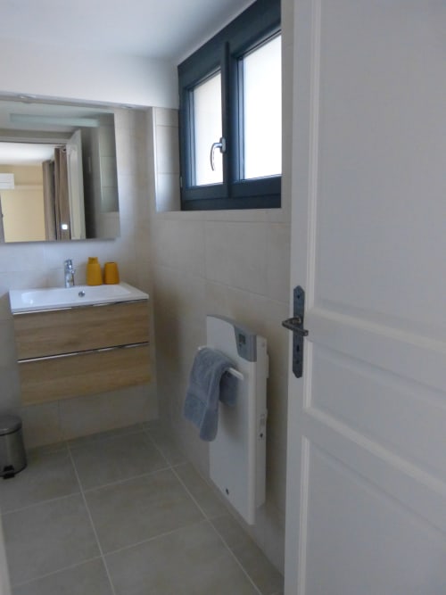 Modern bathroom at Villa Thébaïde with white sink, illuminated mirror, towel warmer, and dark-framed window in Lavande room