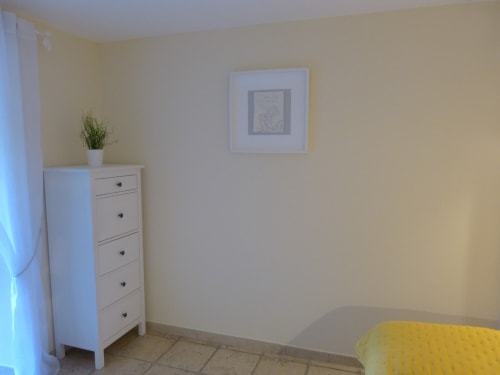 Minimalist bedroom at Villa Thébaïde with white drawer chest, potted plant, framed wall art, and yellow bedding