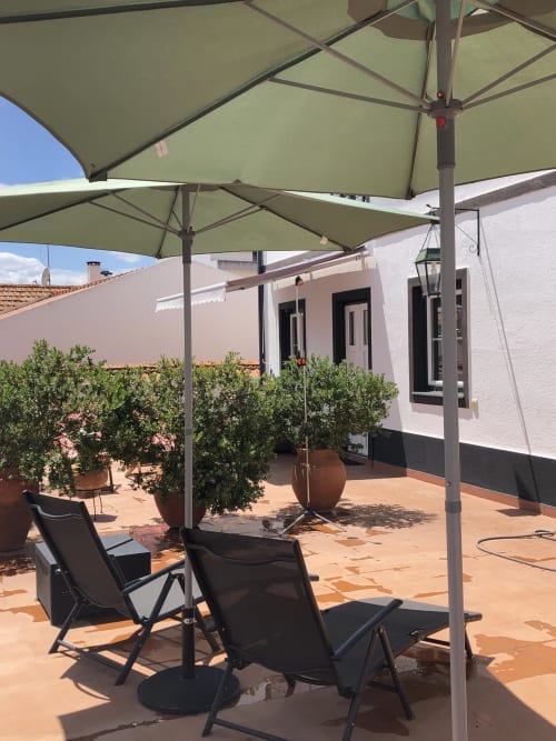 Shaded terrace at Patio Da Villa guesthouse in Coruche with loungers under green umbrellas and potted plants