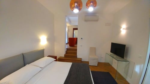 Modern hotel suite bedroom at Stella CasaBono with bed, flat-screen TV, ambient lighting, and wooden floors leading to living