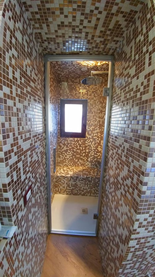 Modern shower stall with mosaic tile walls in brown and cream tones at Stella CasaBono hotel in Sulmona