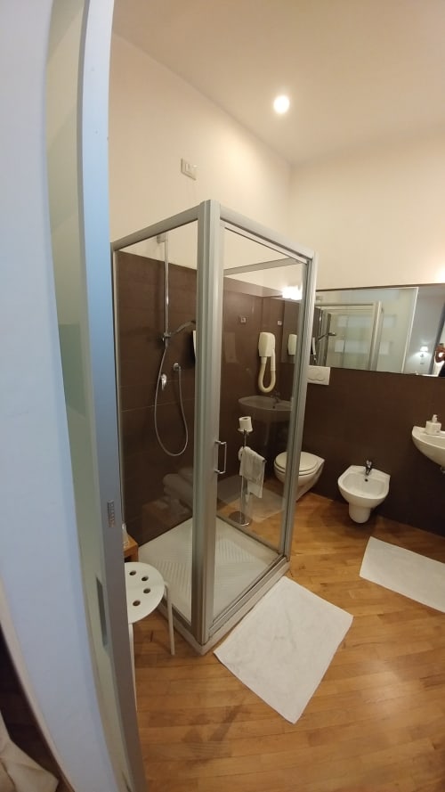 Modern bathroom in Stella CasaBono Junior Suite with glass shower enclosure, dark tile walls, white fixtures, and wooden