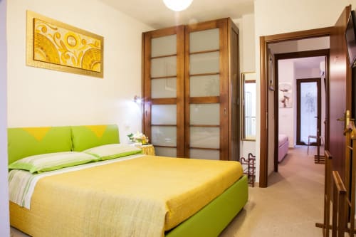 Bright bedroom with lime green headboard, yellow bedding, and wooden wardrobe at Affittacamere Al Mare, Torre Grande Oristano