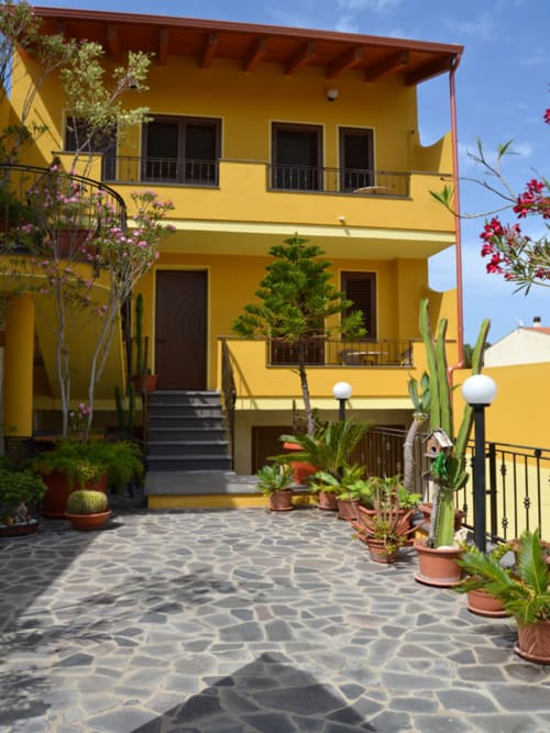 Corte soleggiata di villa mediterranea giallo brillante a Torre Grande Oristano con cactus, piante fiorite e patio in pietra