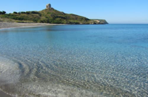 Acque cristalline turchesi e spiaggia sabbiosa a Torre Grande Oristano con rovine di torre storica su verde collina