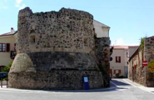 Historic stone tower in Torre Grande Oristano, Italy, featuring medieval architecture with residential buildings nearby