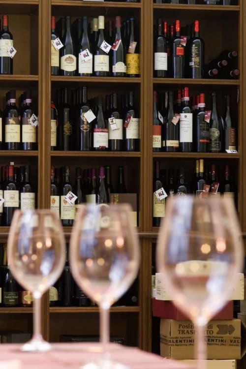 Wine glasses with blurred wine bottles displayed on wooden cabinet shelves at Stella CasaBono hotel in Sulmona