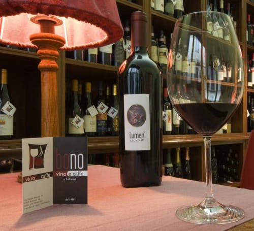 Wine glass with Lumen wine bottle at Stella CasaBono wine bar in Sulmona, Italy, with red lamp and wine bottles displayed