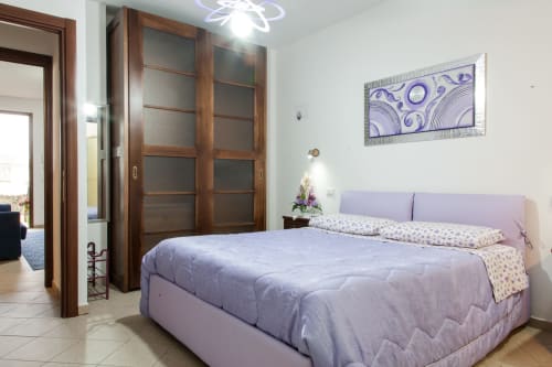 Chambre lumineuse avec lit double violet, armoire en bois et décoration moderne à Affittacamere Al Mare à Oristano, Italie