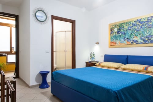 Camera moderna presso Affittacamere Al Mare con letto blu, mobili in legno, specchio decorativo e quadri incorniciati a Torre