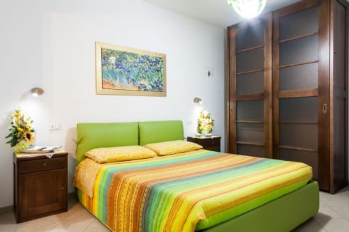 Chambre lumineuse avec lit vert anis, linge de lit aux rayures colorées, armoire en bois et œuvres d'art encadrées à l'Affittacamere Al Mare